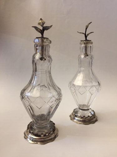Pair early 18th century cut glass condiment bottles with silver plated mounts and leaf formed stoppers.